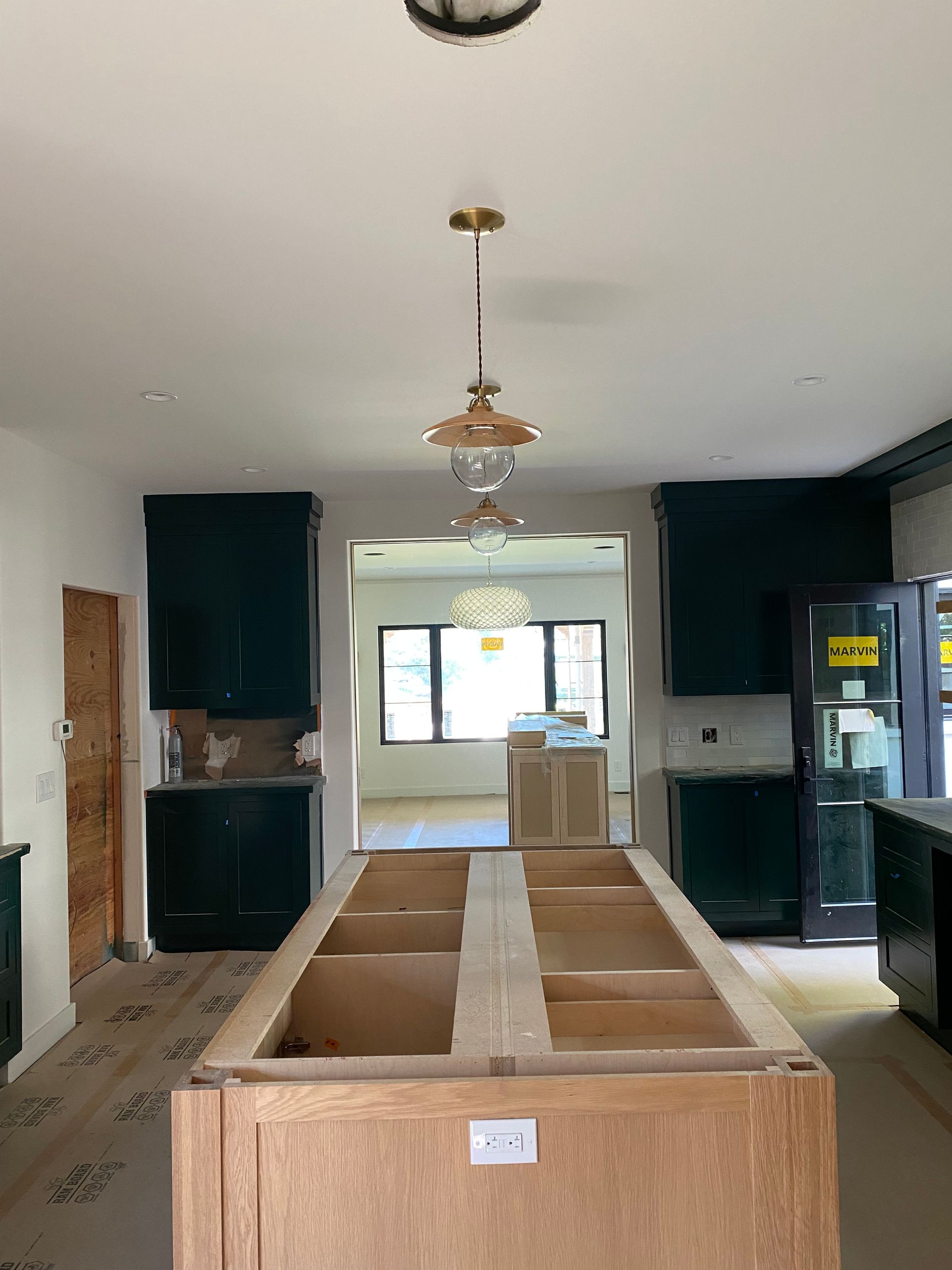 Kitchen under construction with green cabinets, wood island, and pendant light fixture.