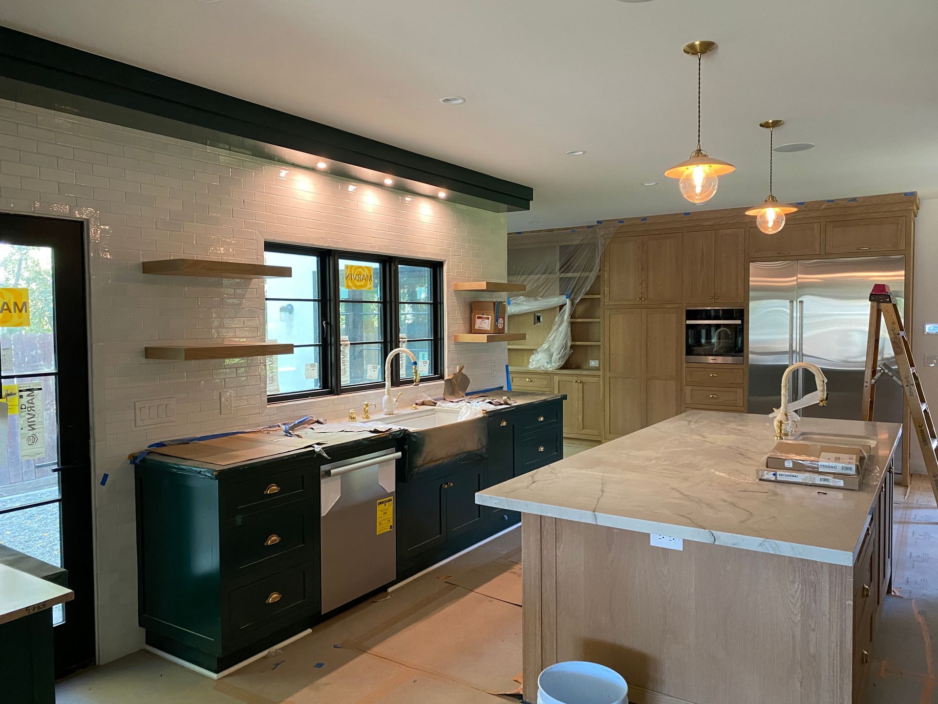 Kitchen under construction with green cabinets, white backsplash, and wooden island.