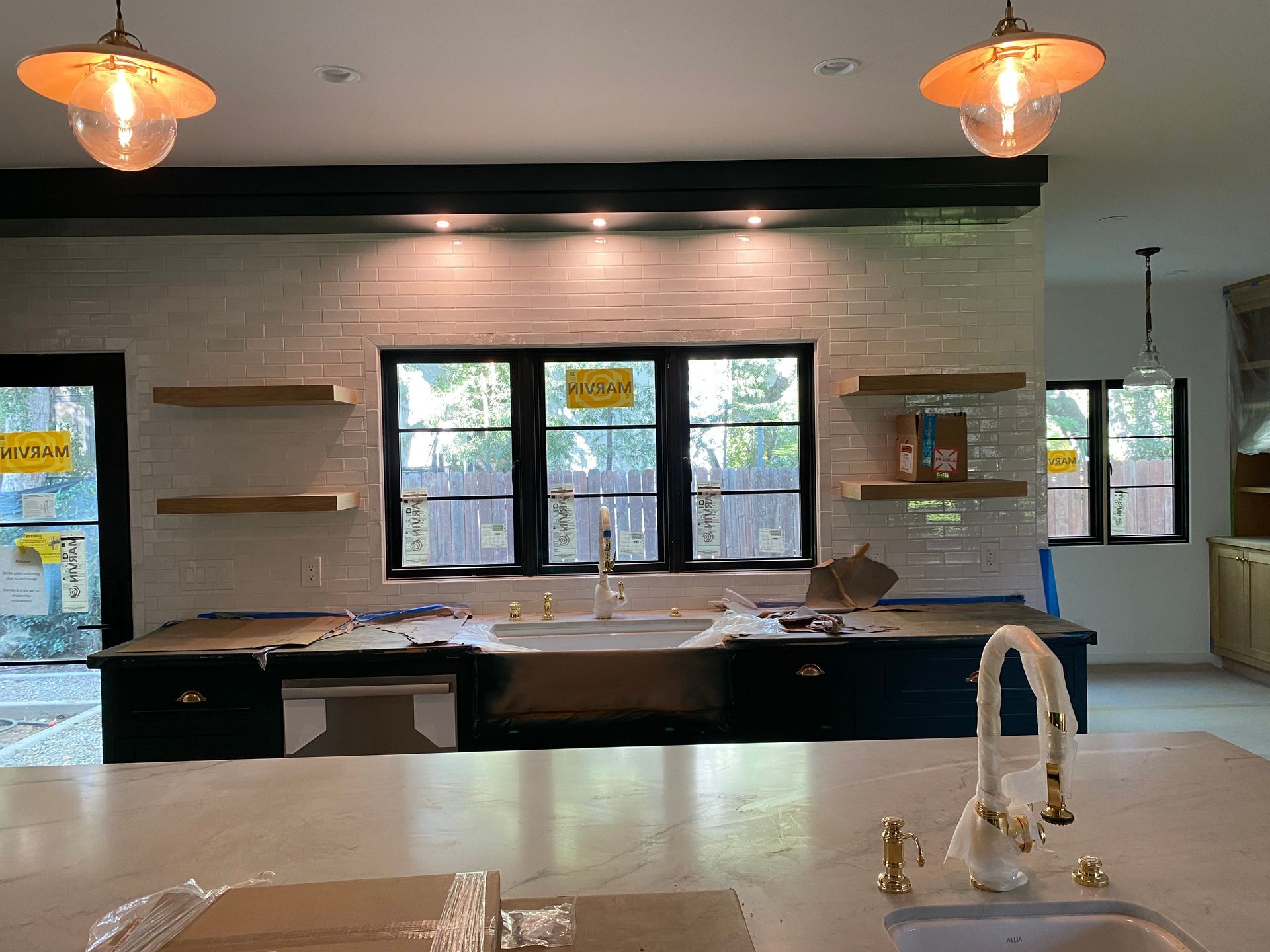 Kitchen with farmhouse sink, black windows, white brick backsplash, wood shelves, and pendant lights.