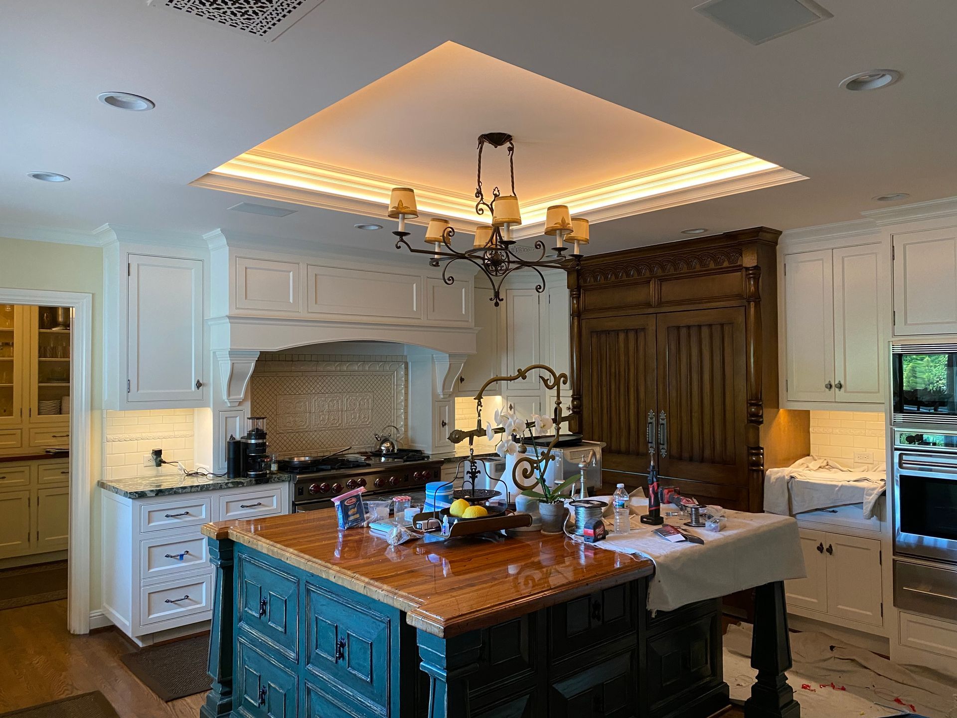 Kitchen with white cabinets, a teal island, a chandelier, and a decorative ceiling.