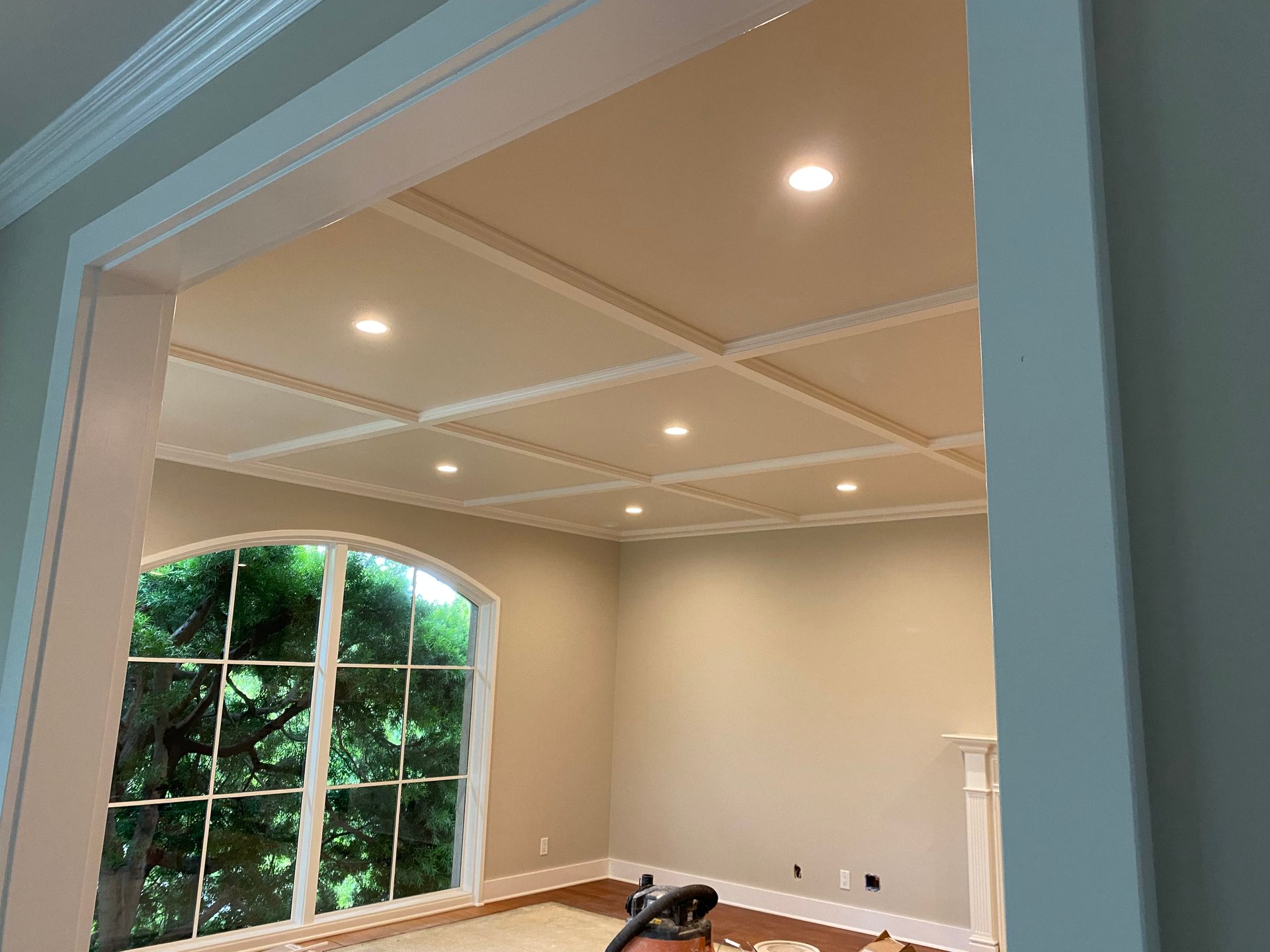 Room with coffered ceiling, recessed lights, arched window, and beige walls.