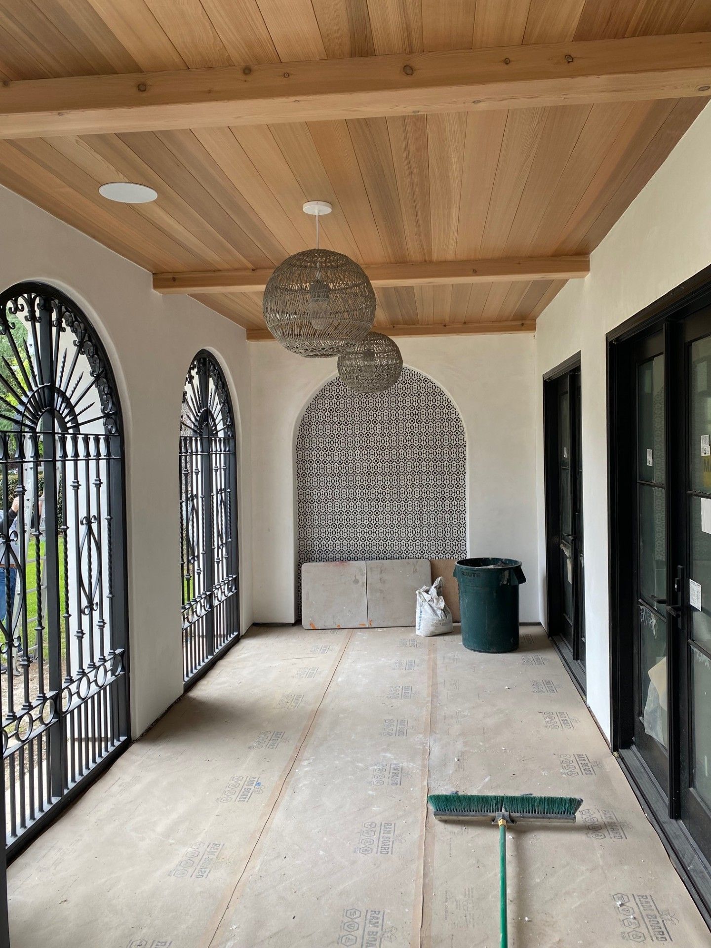Covered patio with arched windows and doors, wood ceiling, patterned tile wall, and unfinished concrete floor.