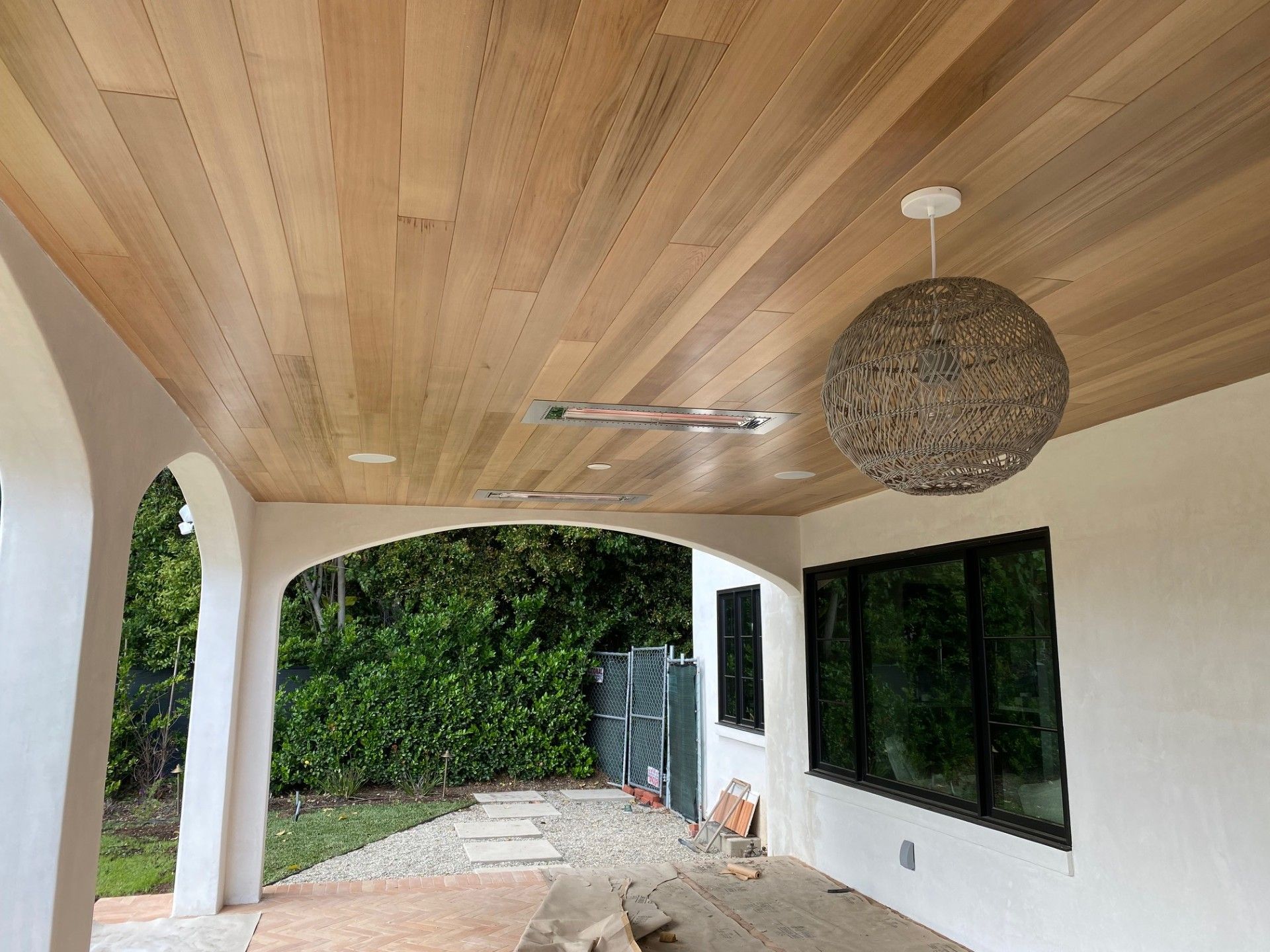 Wooden ceiling on a covered patio with an arched entryway. A pendant light hangs from the ceiling. Dark windows.