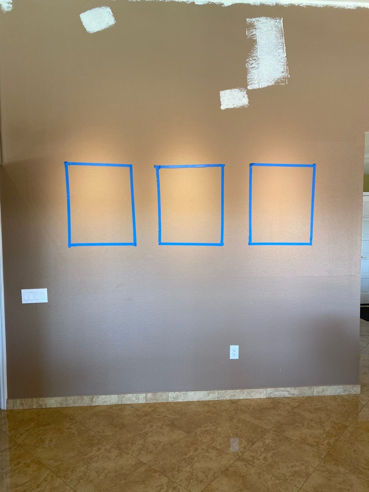 Brown wall with three taped squares, a light floor, and paint swatches at the top.