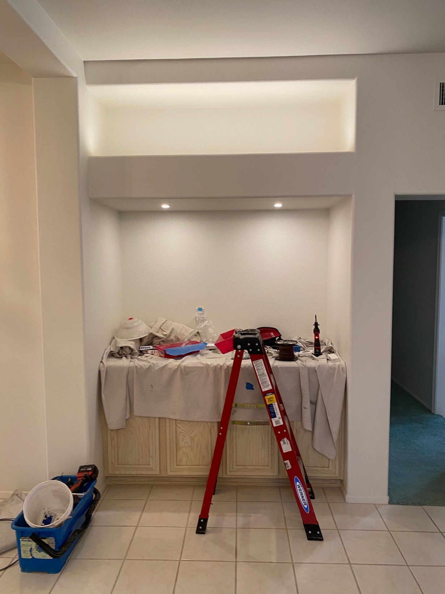Interior renovation: alcove with recessed lighting, cabinet, ladder, tools, and paint supplies.