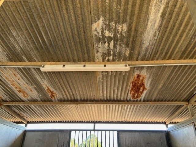 Interior view of a corrugated metal roof with rust and a mounted light fixture.
