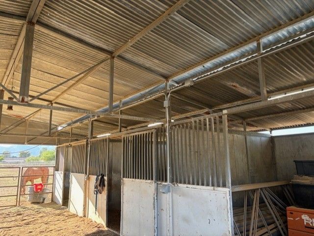 Inside view of metal horse stables under a corrugated metal roof.