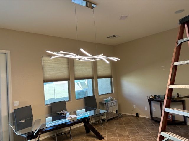 Dining room with a modern chandelier over a glass table; a ladder is to the right.