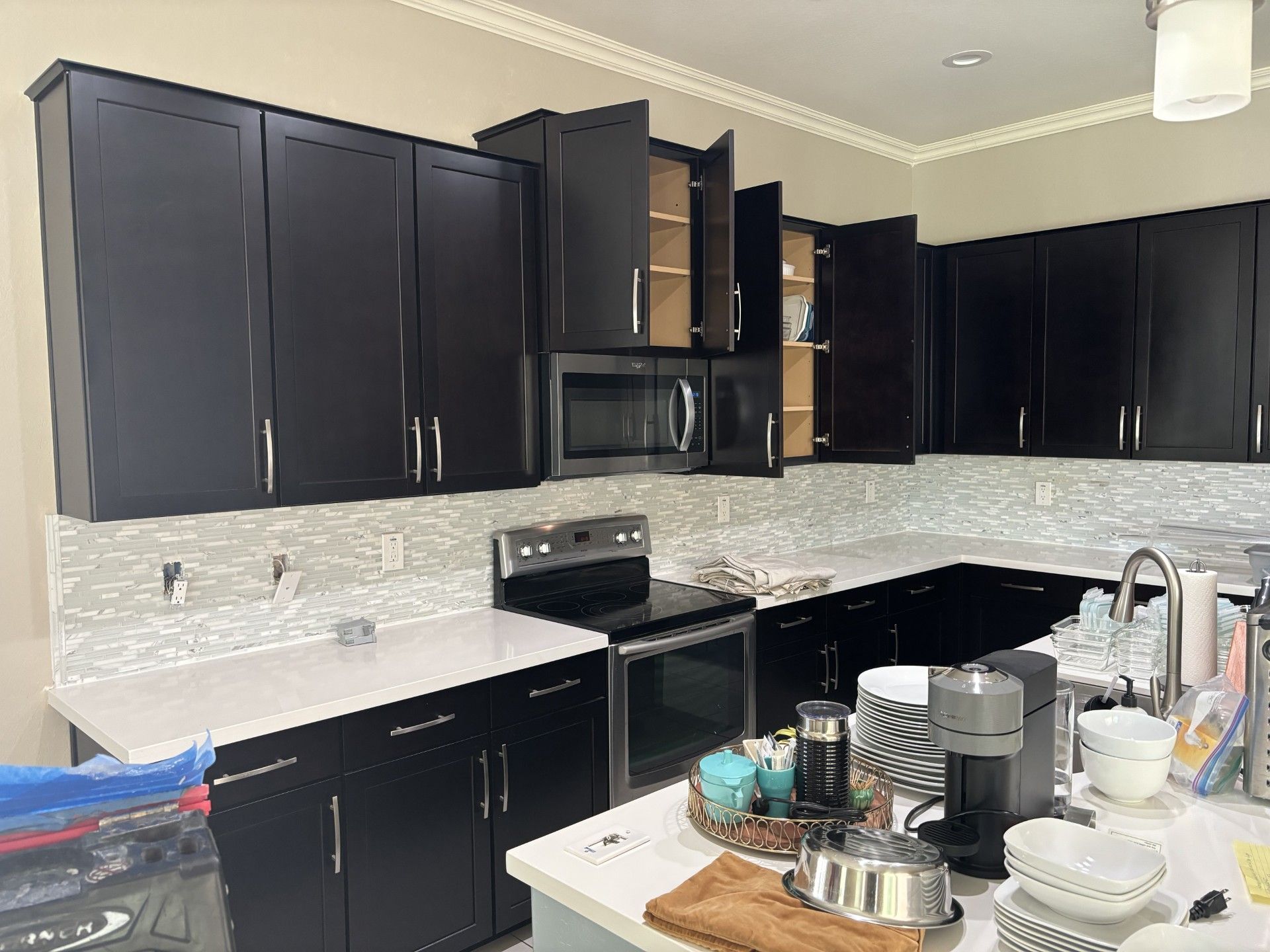 Black kitchen cabinets with white countertops, backsplash, and appliances. Some cabinet doors are open.