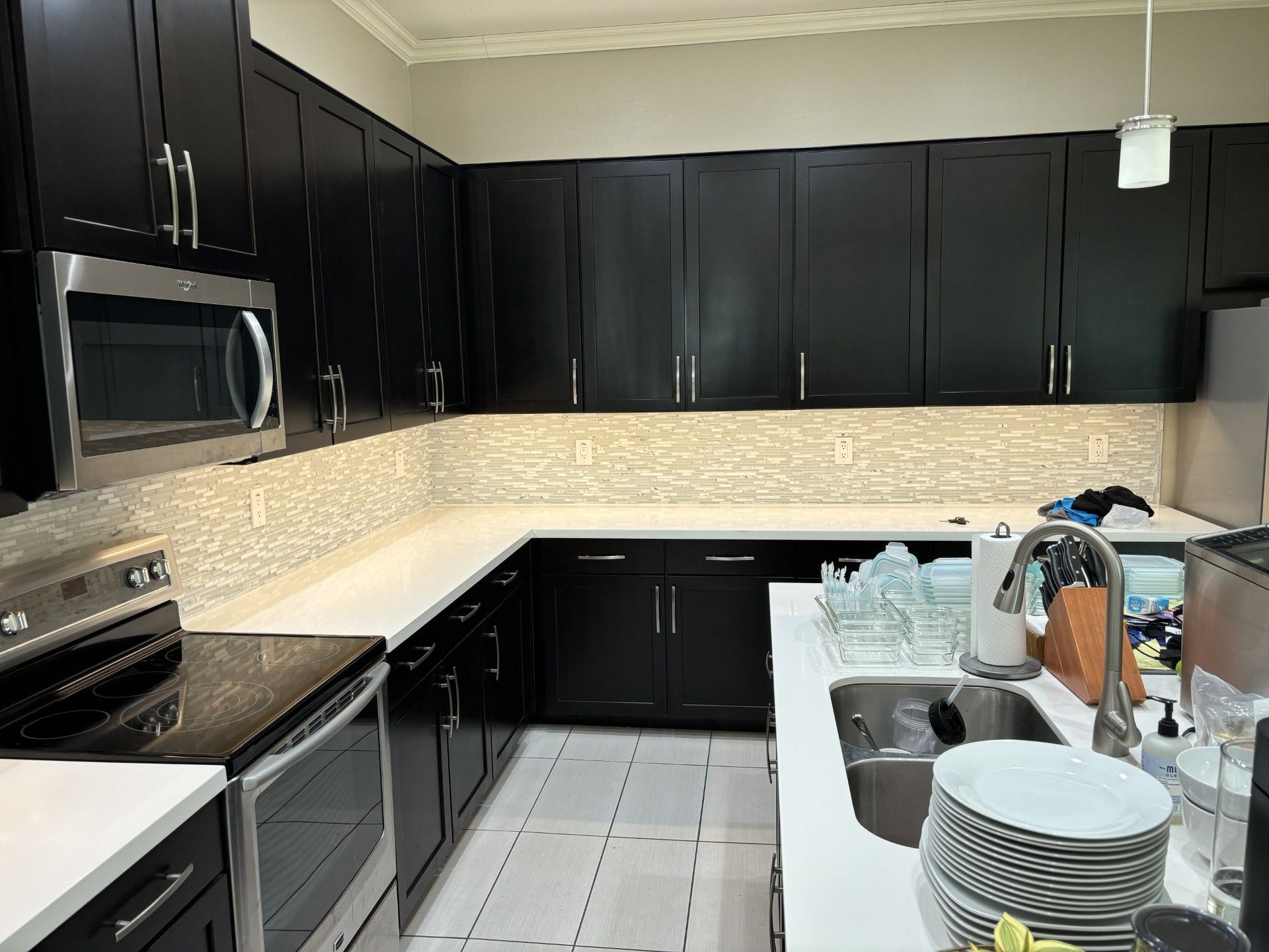 Kitchen with black cabinets, white countertops, stainless steel appliances, and a light-colored backsplash.
