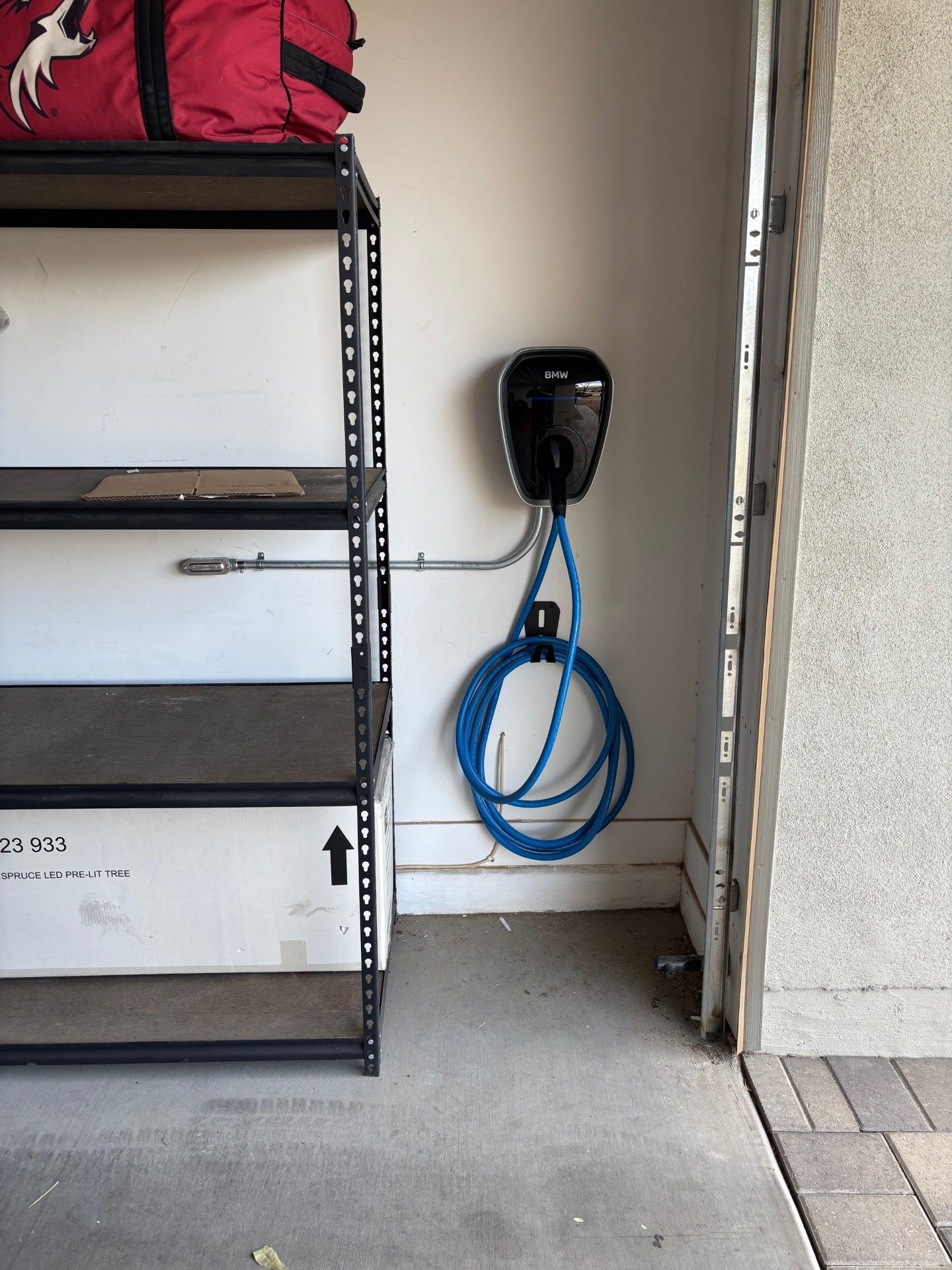 Electric vehicle charger mounted on a garage wall, blue cable coiled below. Next to a shelf unit.