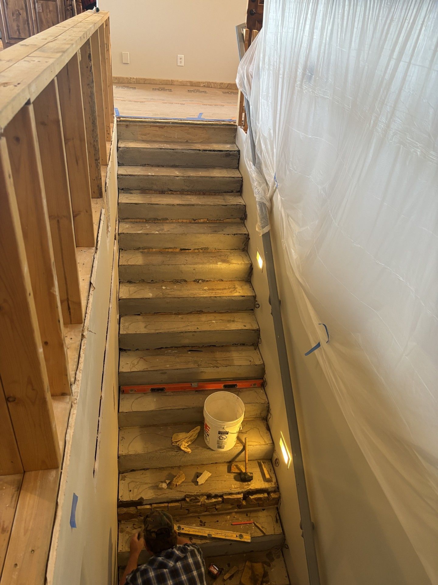 Staircase under construction; person at bottom, white sheeting on right, wood framing on left.