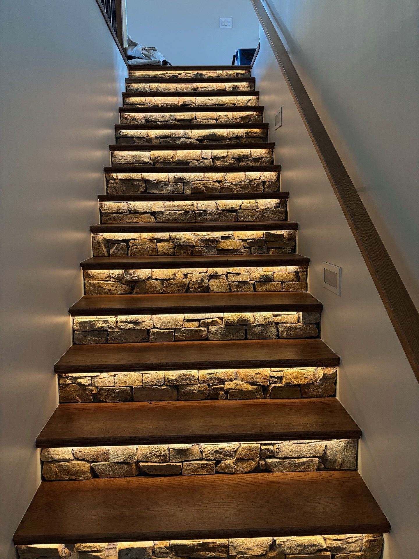Staircase with wooden steps and stone risers, illuminated with LED lighting.
