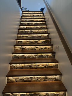 Staircase with brown wooden steps, stone risers, and LED lighting illuminating each step in a neutral setting.