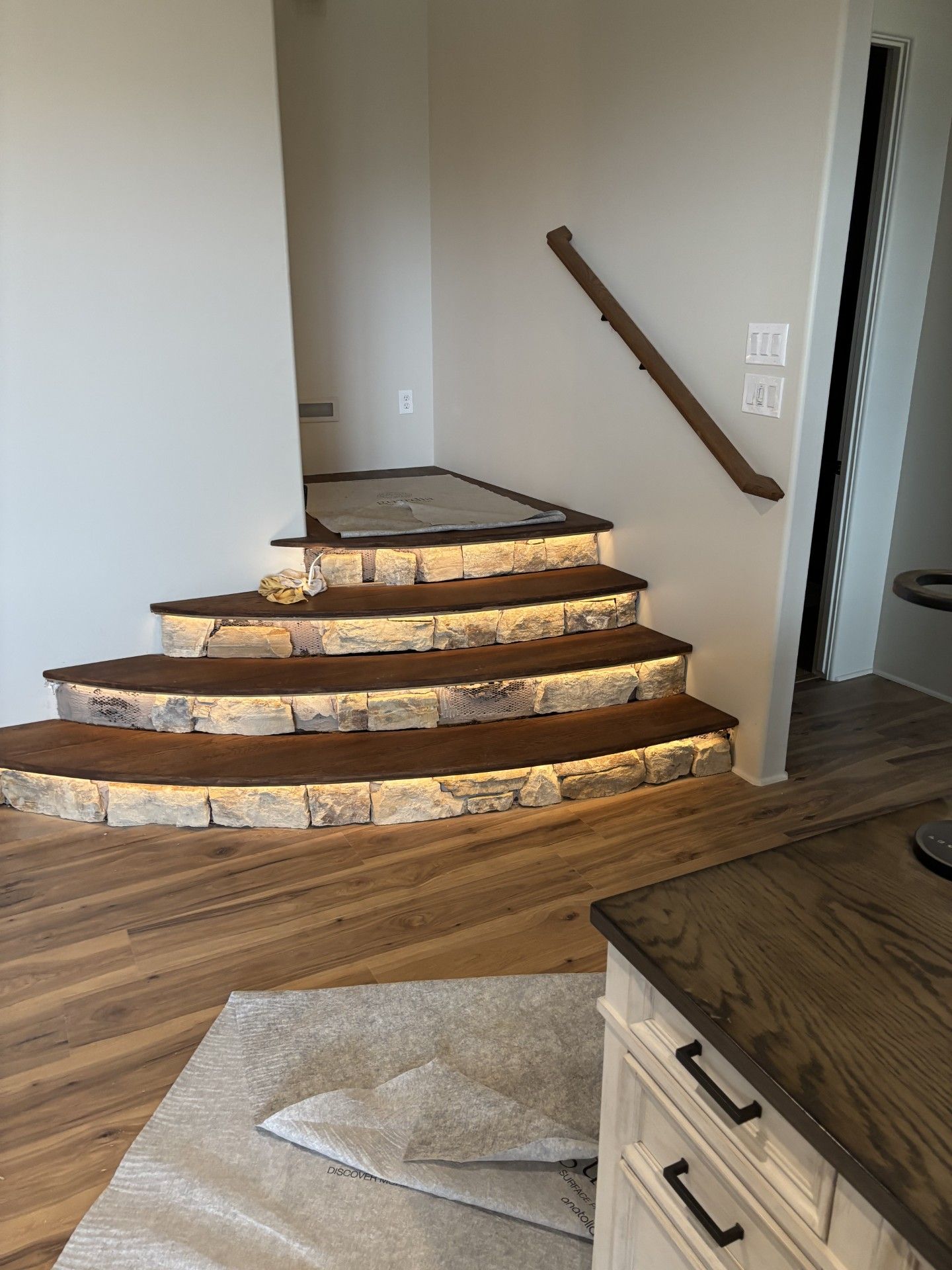 Staircase with built-in lights, brown steps, stone accents, wood flooring, and a handrail.