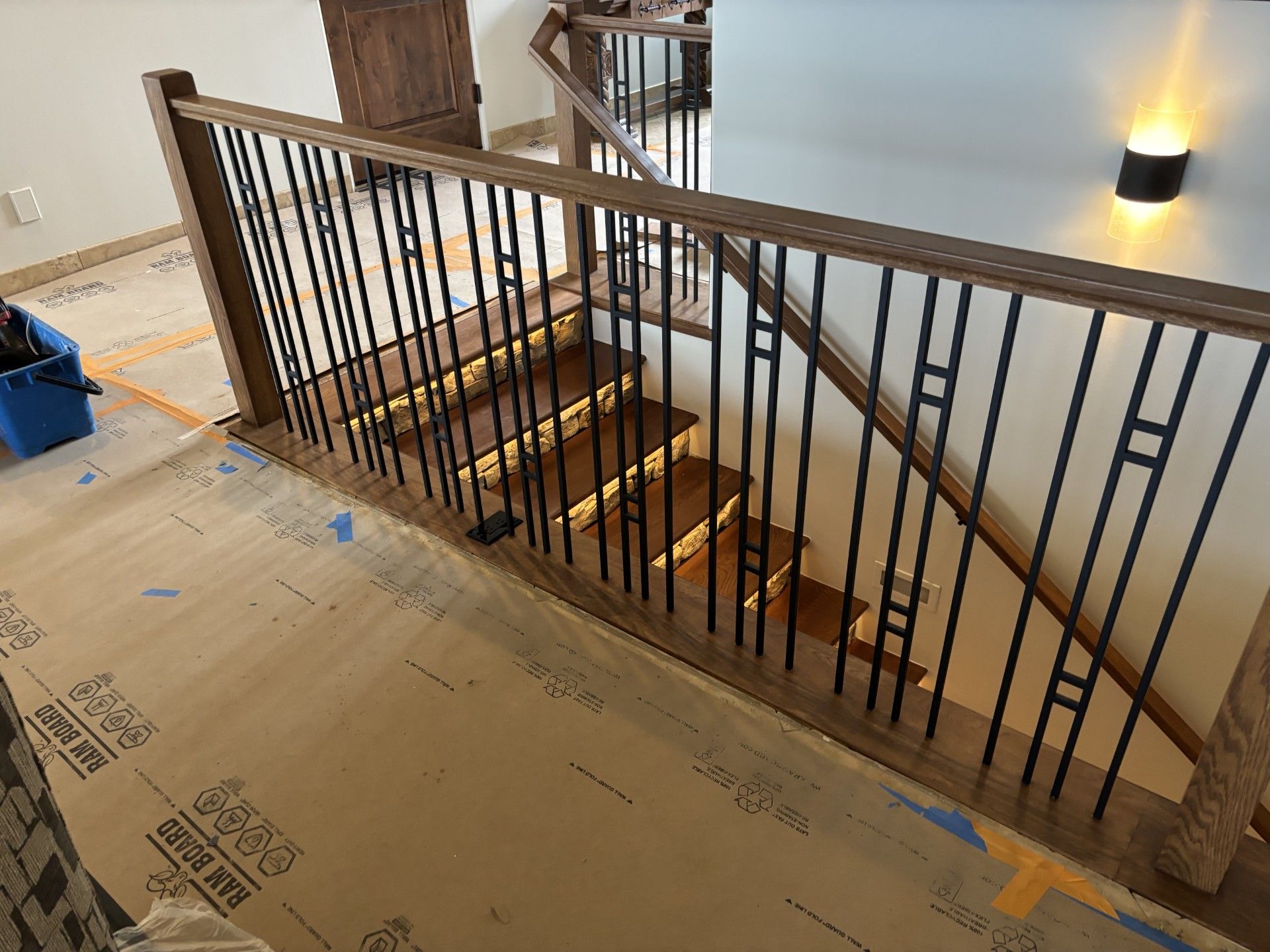 Wooden staircase with black metal balusters, lit stairs, and protective floor covering.