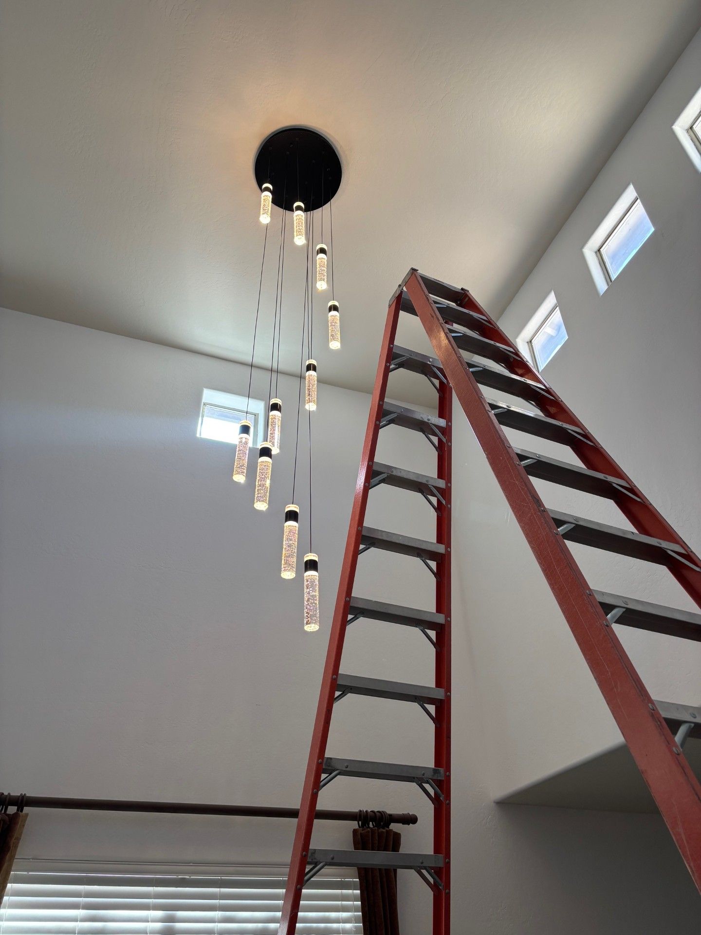 Red ladder next to a modern chandelier fixture against a white wall.