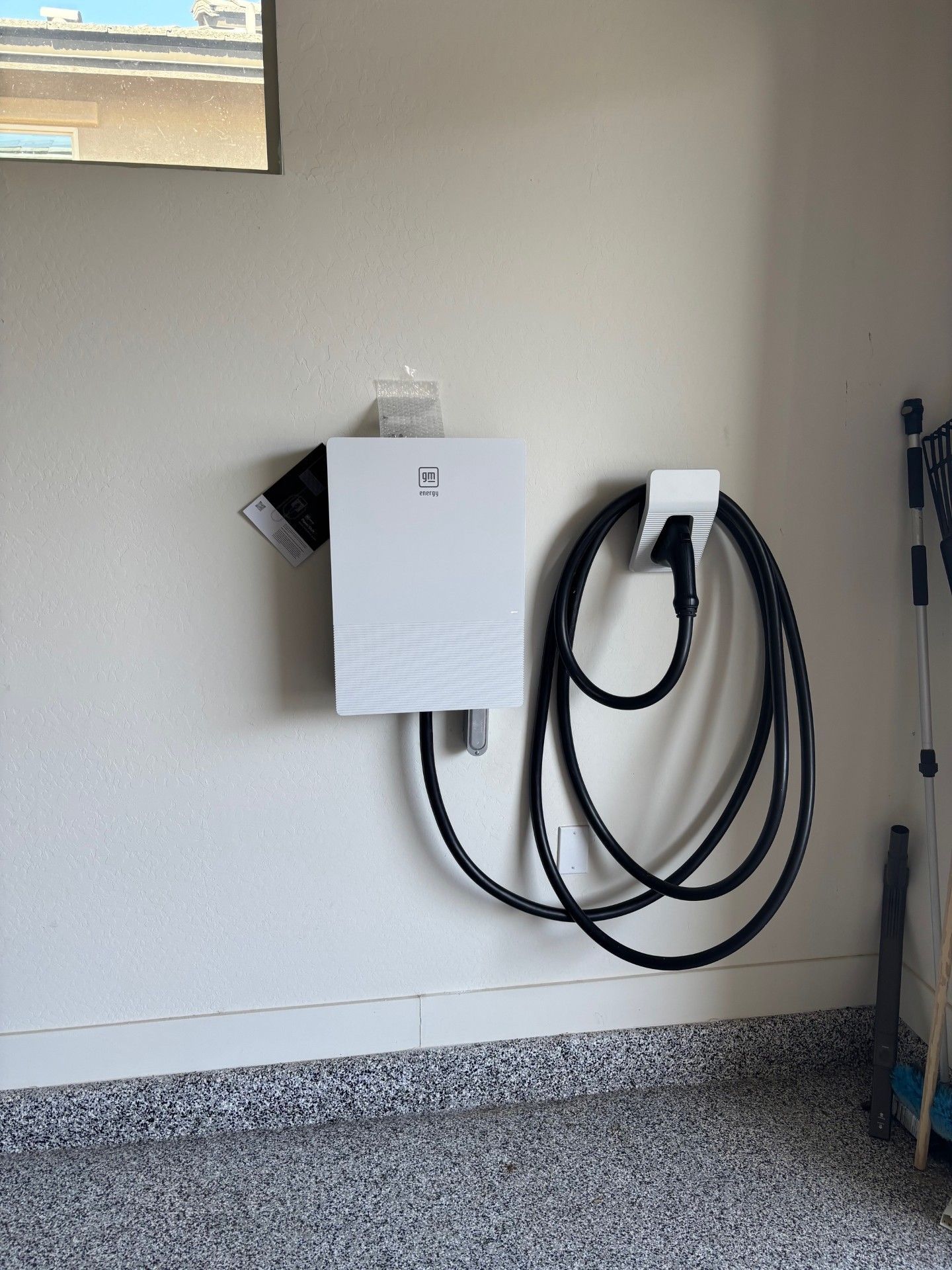 White electric vehicle charger mounted on a garage wall with coiled black cable and charging head.