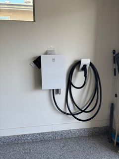 White electric vehicle charger mounted on a garage wall, with a coiled black cable.