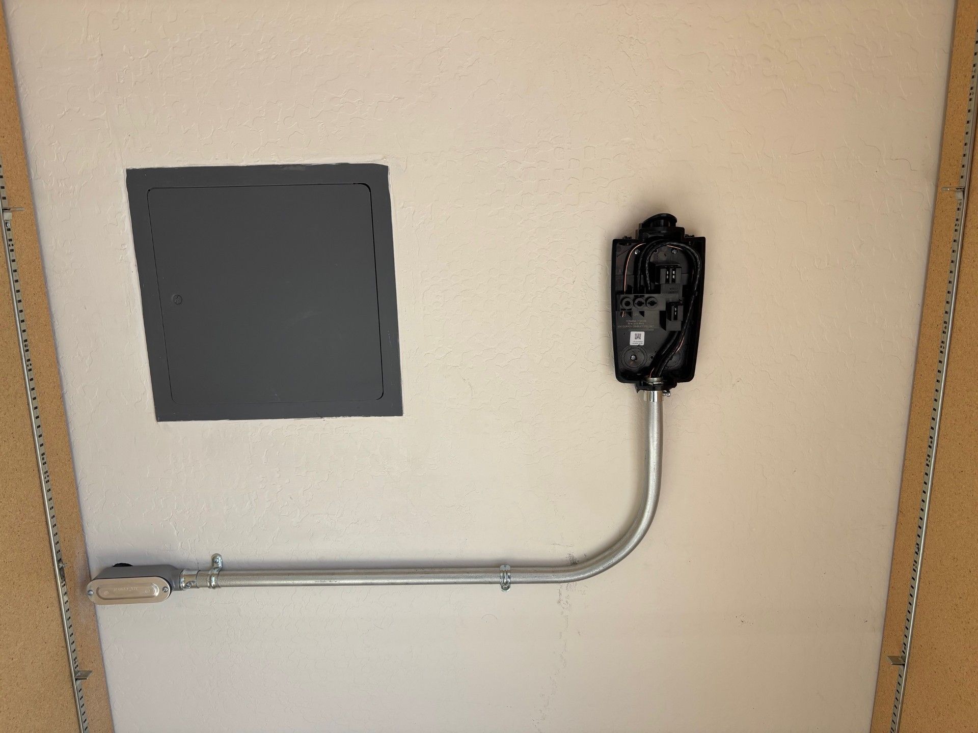 Electrical panel and EV charger mounted on a light-colored wall, with conduit running between them.