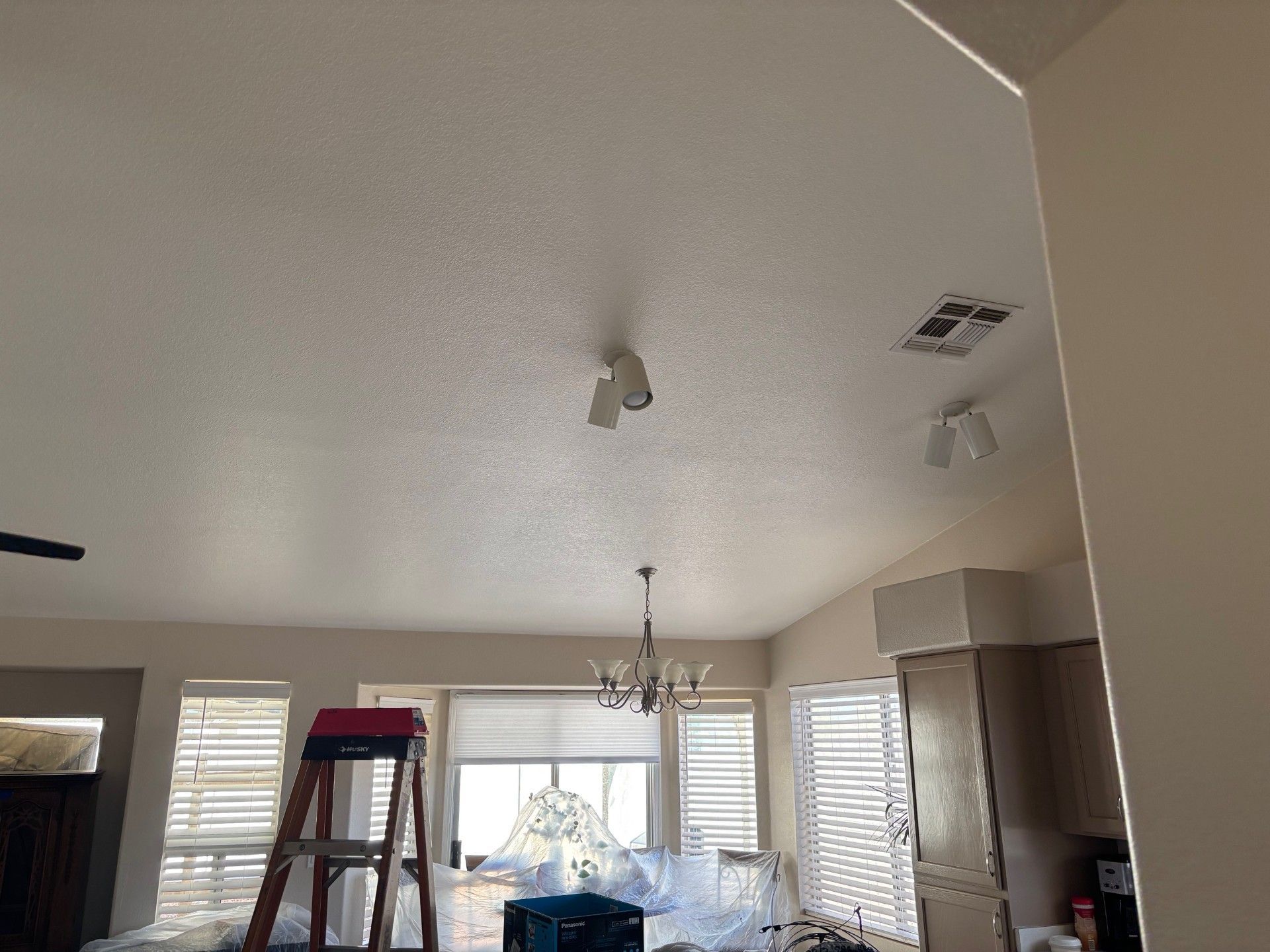 Interior view of a room with popcorn ceiling, lights, and a ladder.