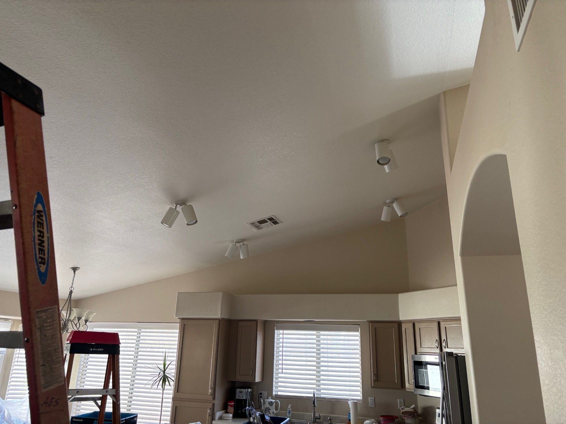 A-frame ceiling with recessed lighting above kitchen cabinets, a ladder leans against the wall.