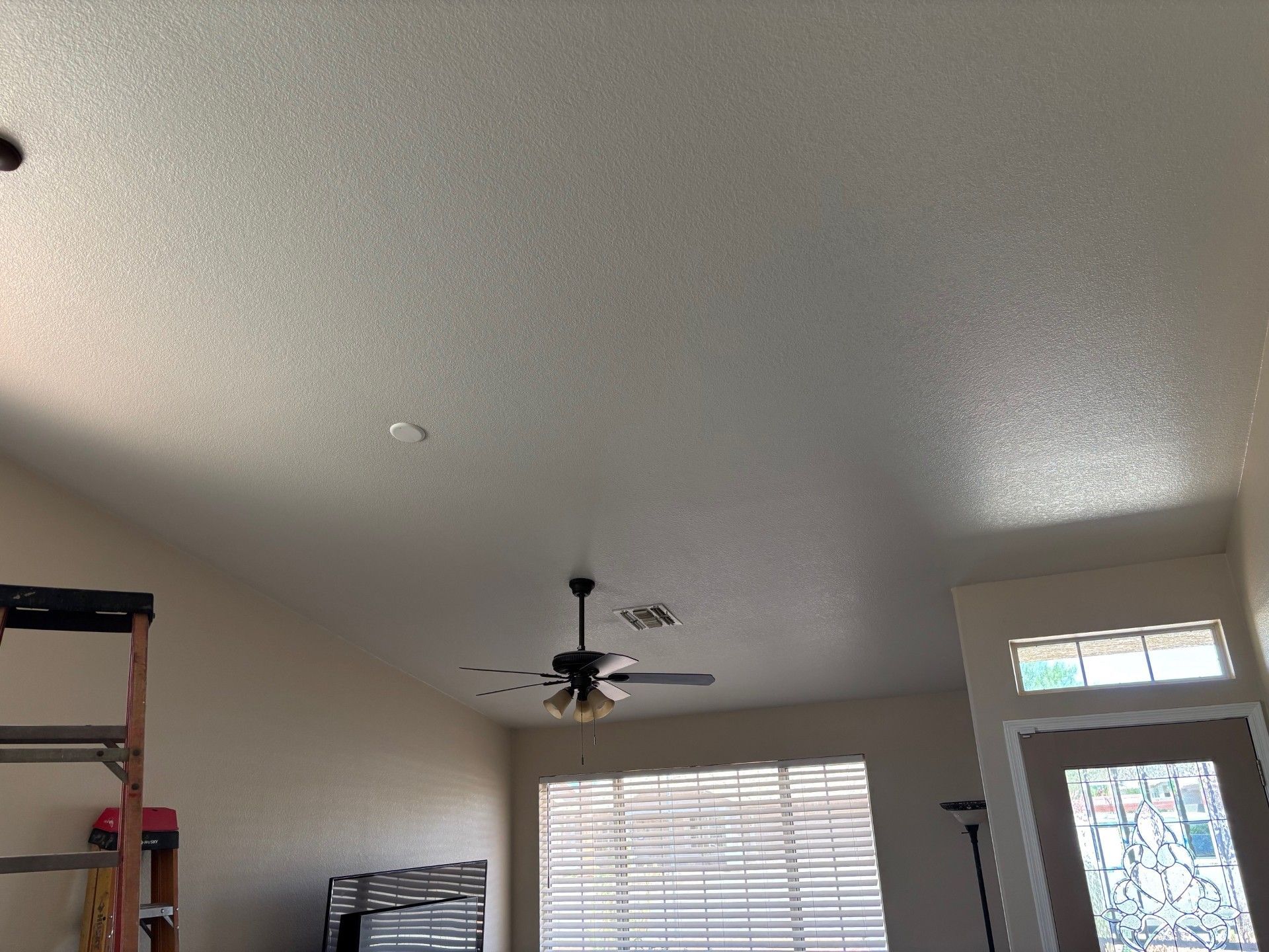 Interior view of a room with a textured ceiling, a ceiling fan, windows, and a doorway.