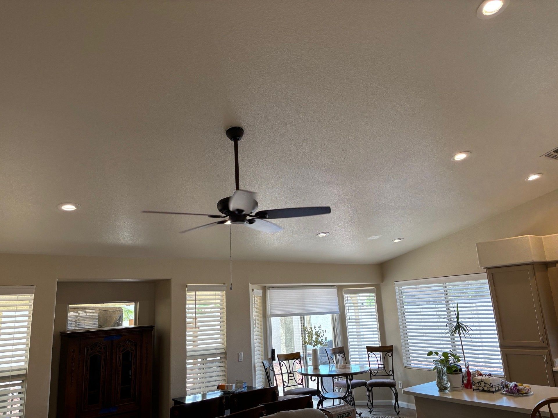 Ceiling fan in a room with recessed lights and window blinds. Neutral-colored walls.