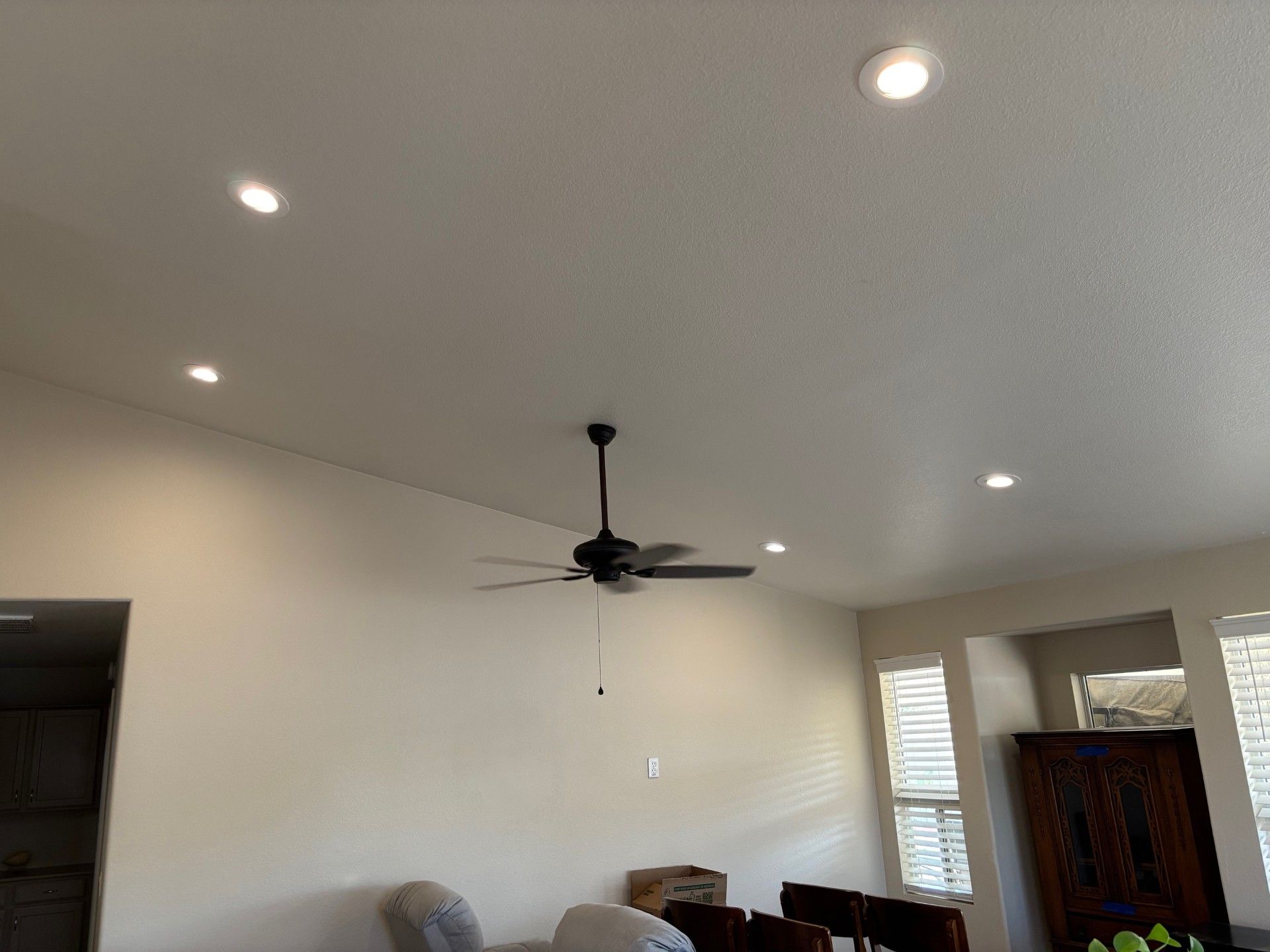 Ceiling with recessed lights and a ceiling fan; white walls and a dark wooden cabinet in the background.