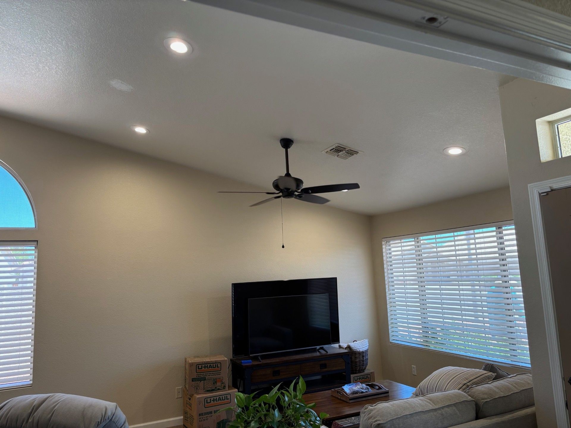 Living room with TV, ceiling fan, recessed lights, and window blinds.