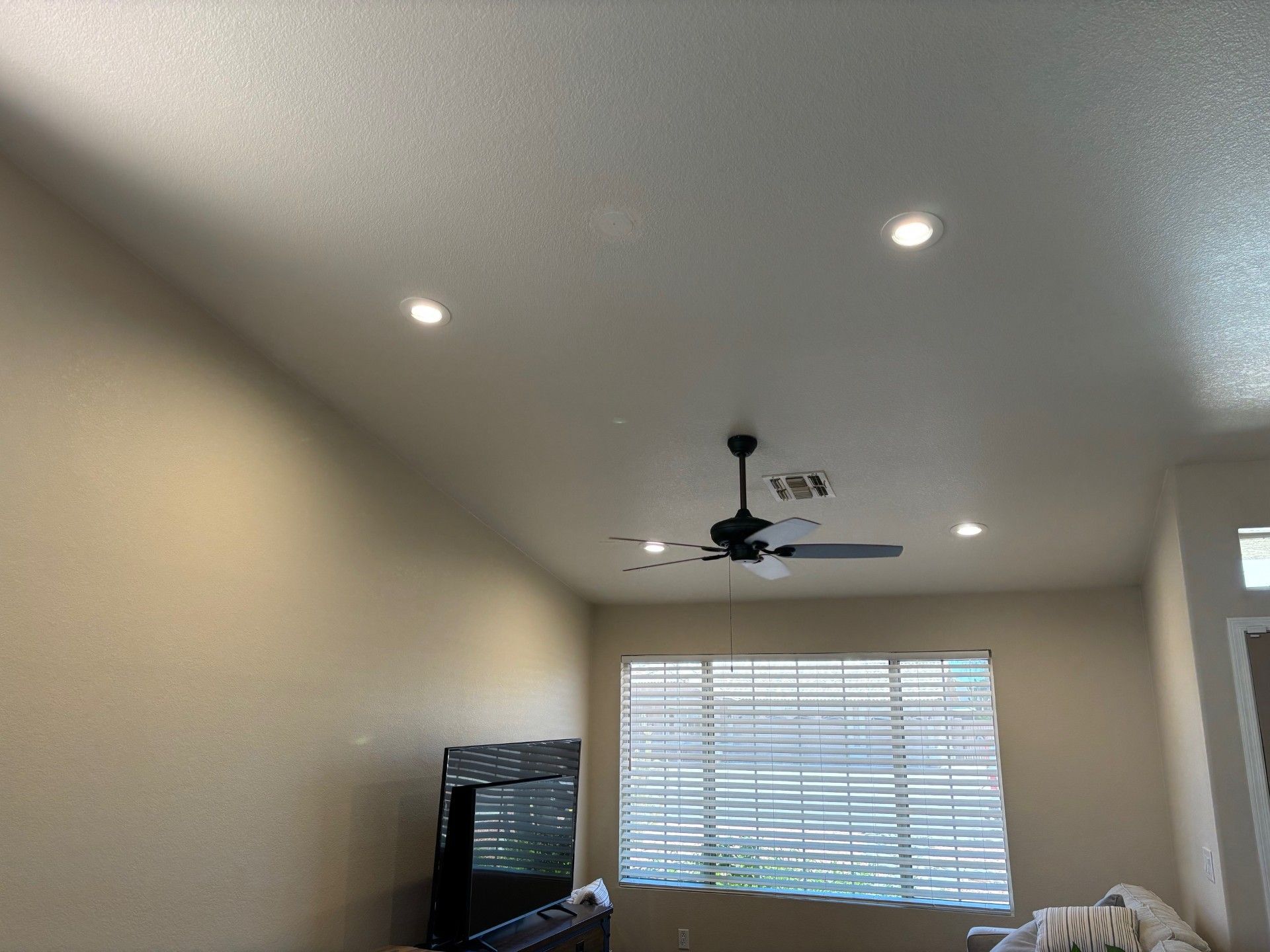 Living room with recessed lights, ceiling fan, TV, and window with blinds.