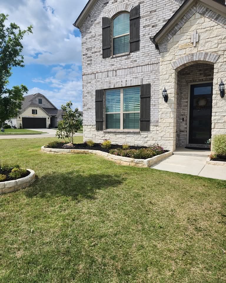 A two-story brick and stone house with dark shutters, a front yard with landscaped stone beds, and a driveway.