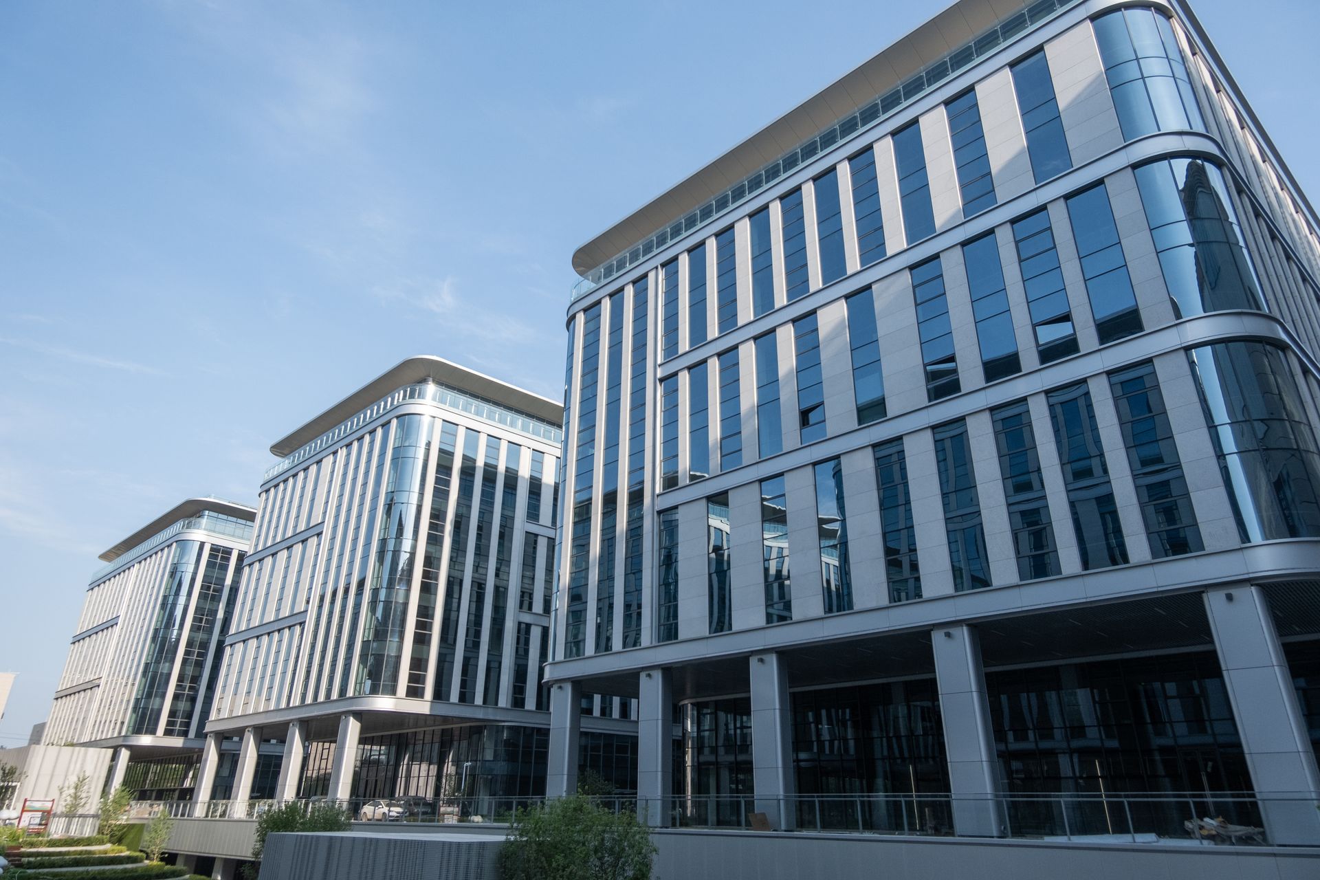 Three modern office buildings with glass and gray facades under a blue sky.