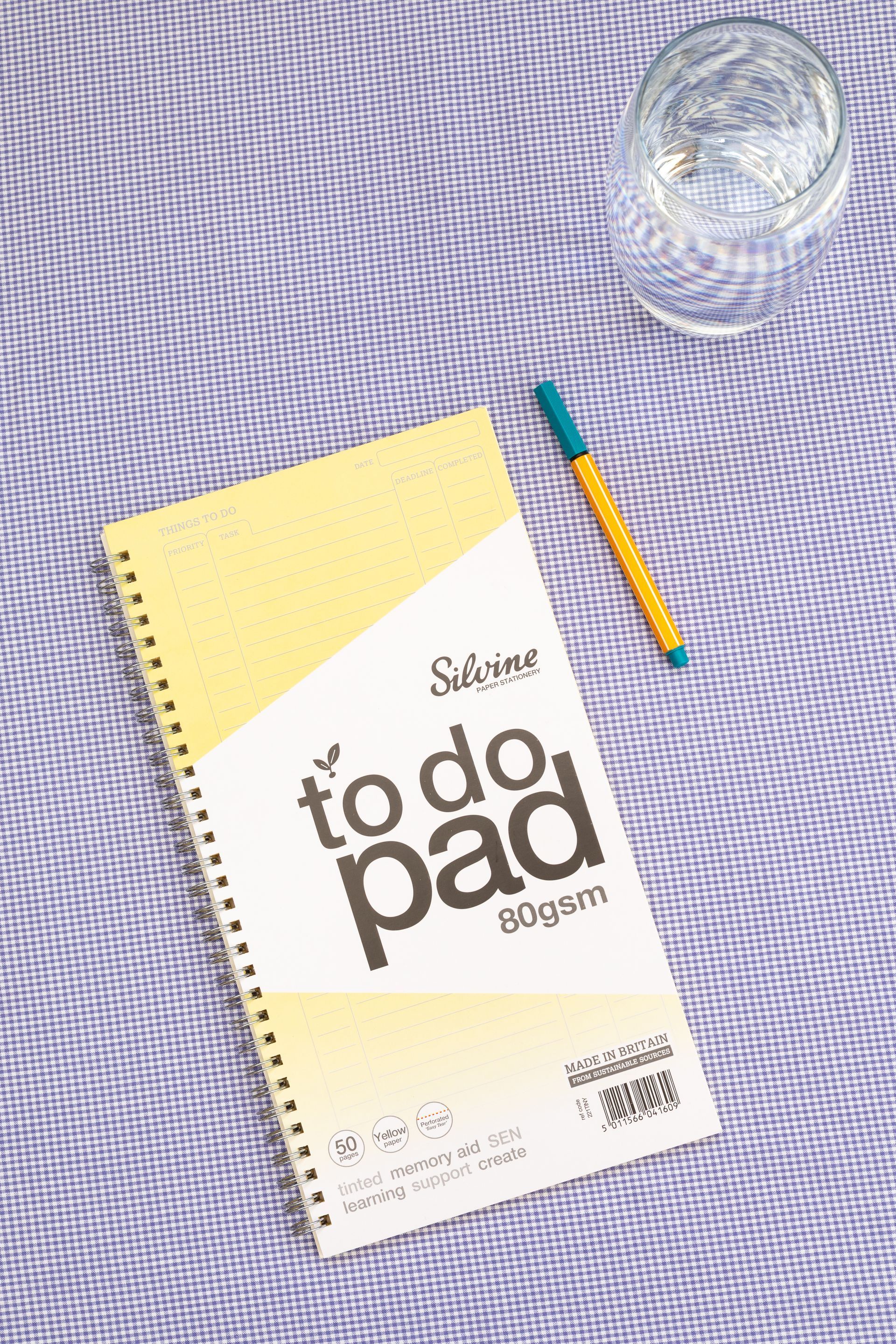 Yellow Tinted To Do List Pad on a purple gingham background with a pen to the side of it.