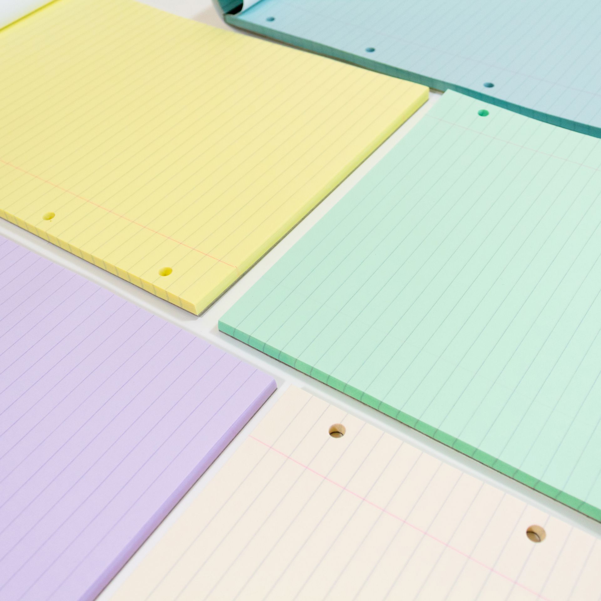 Tinted paper refill pads placed on a white background and laid with papers open to reveal paper tints. Colours purple, yellow, blue, green and cream are on show. 