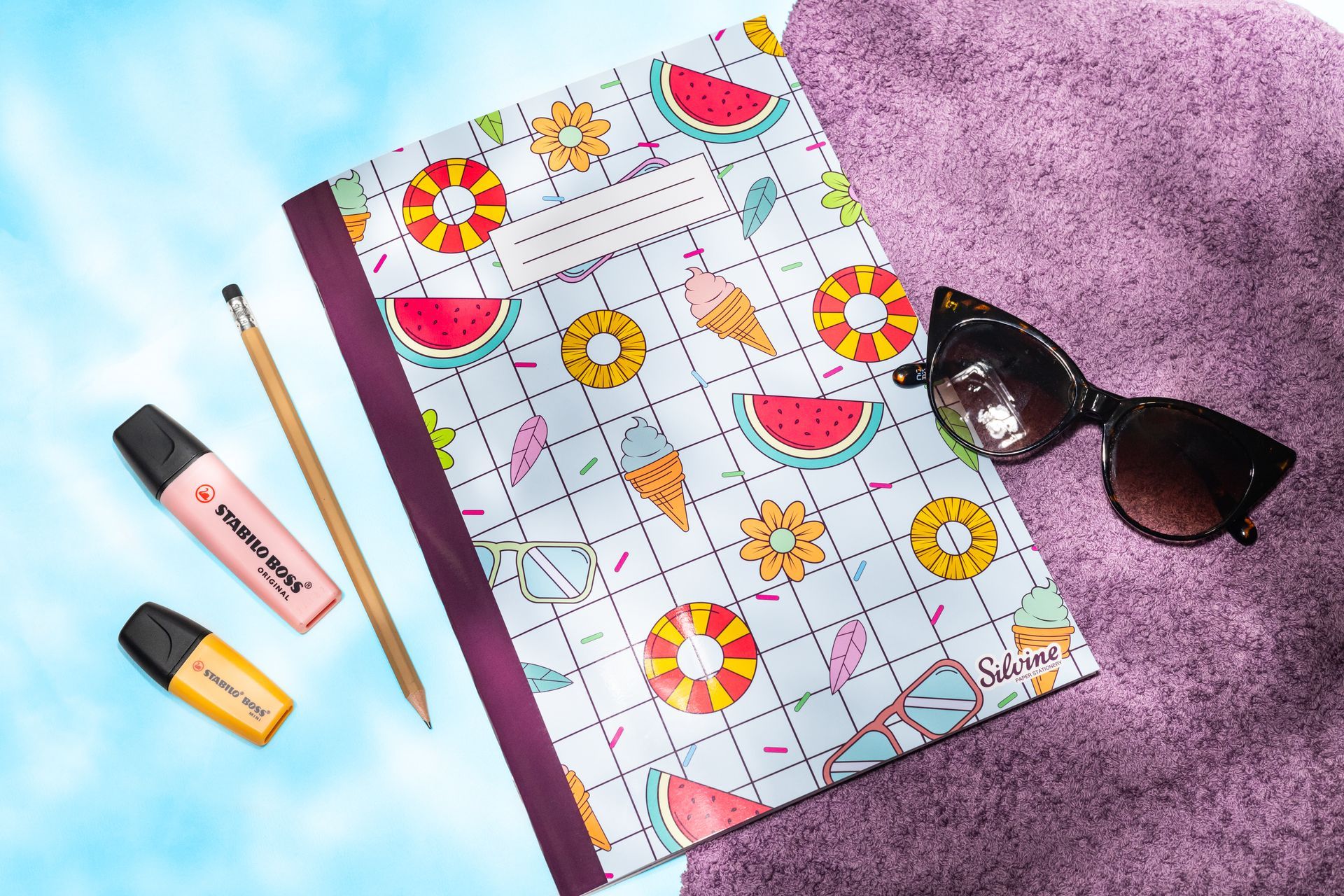 Exercise book by Silvine with Pool Party design on the cover. It is by a swimming pool with highlighters, sunglasses, pencil and purple towel.
