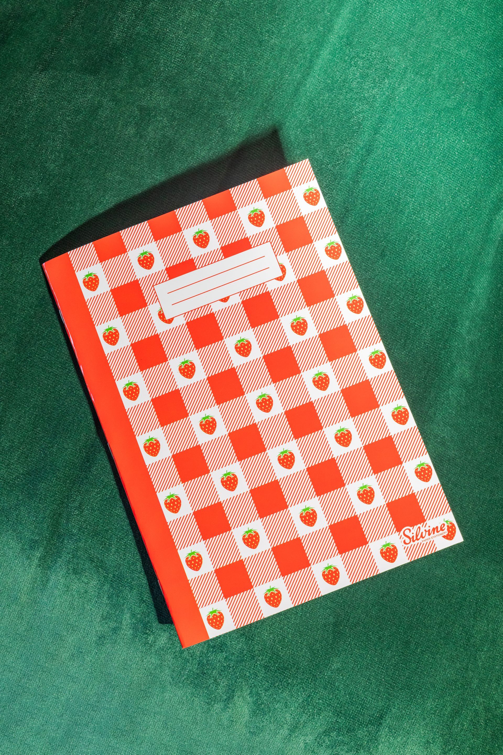 Exercise book by Silvine with Strawberries design on the cover. It is on a green background.
