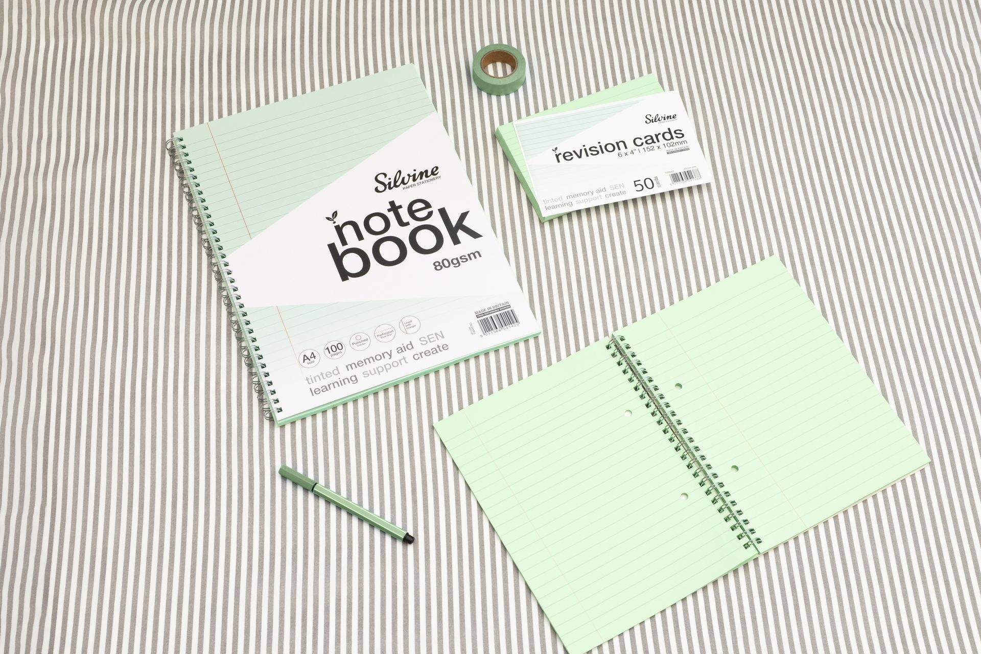 Green tinted notebook, revision card pack and green stationery accessories on a grey lined background.