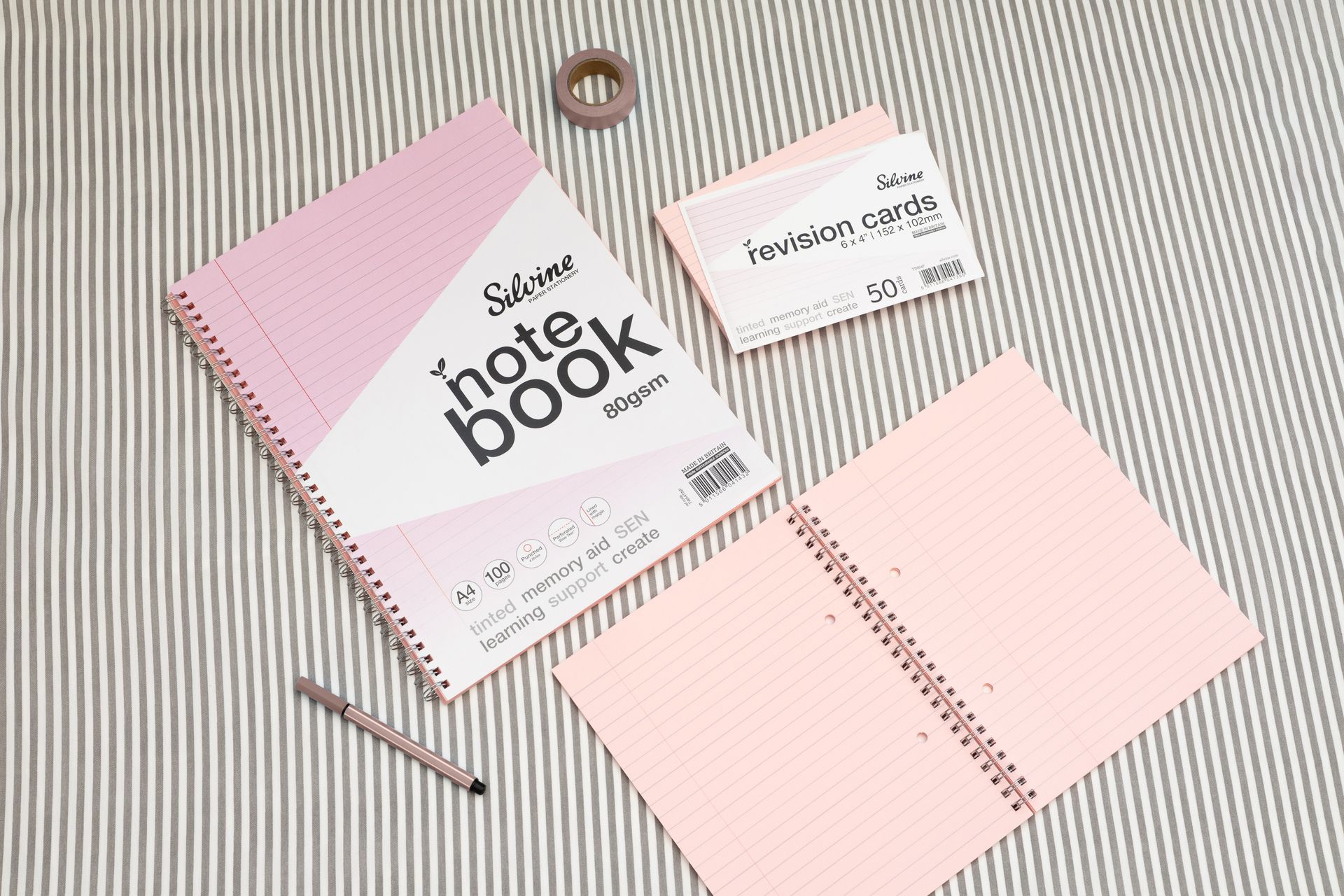 Pink tinted notebook, revision card pack and pink stationery accessories on a grey lined background.