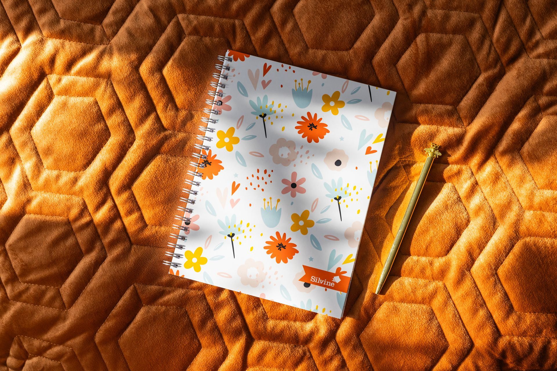 A Silvine Fashion Notebook with pen on a textured throw with the sun shining upon it.