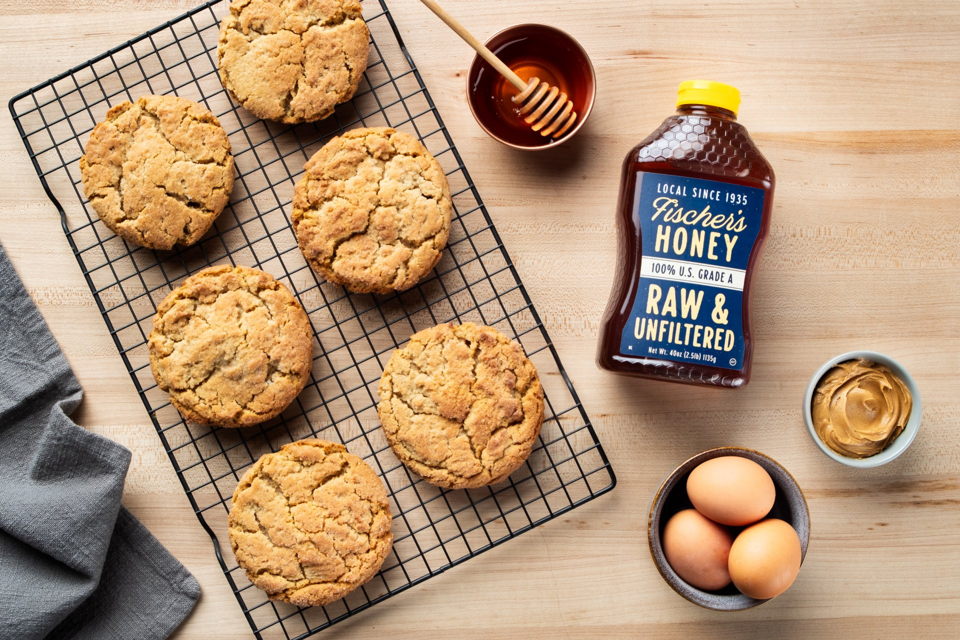 photo of freshly baked peanut butter cookies on a butcher block counter top with a bottle of fischer's raw and unfiltered honey laying next to them