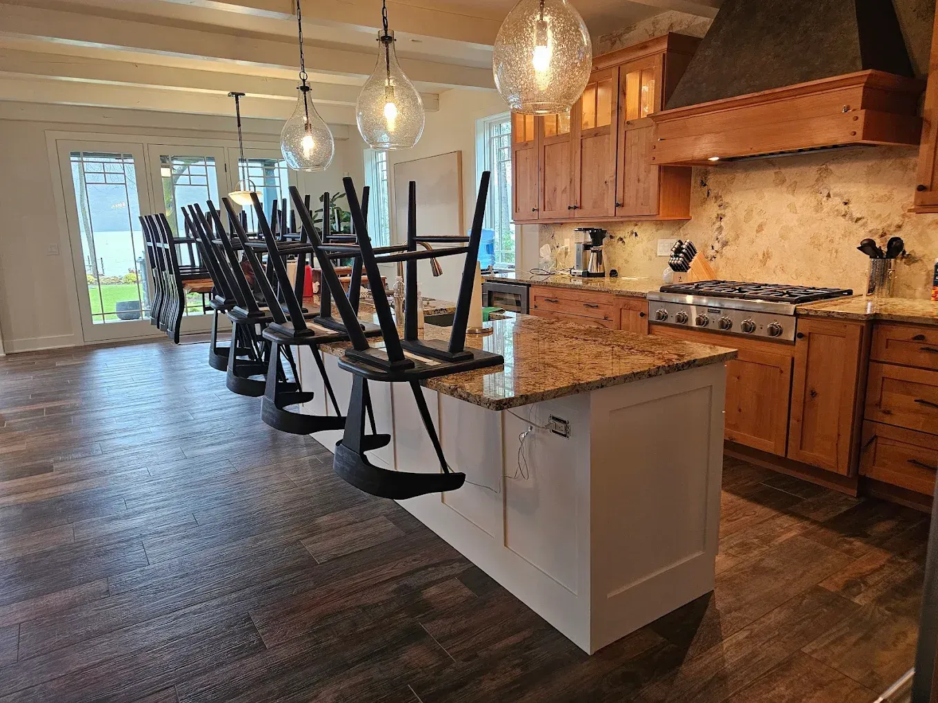 Kitchen with island and chairs upended on it. Wooden cabinets, granite countertops, and pendant lights.
