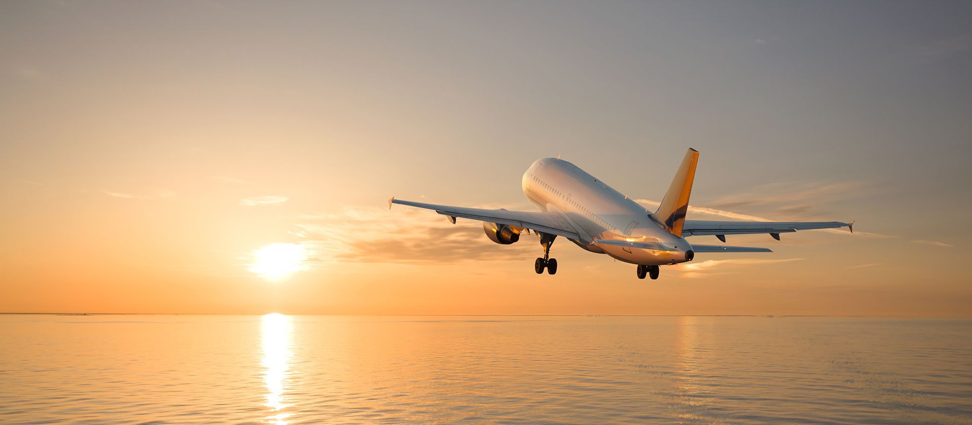An airplane is flying over the ocean at sunset.