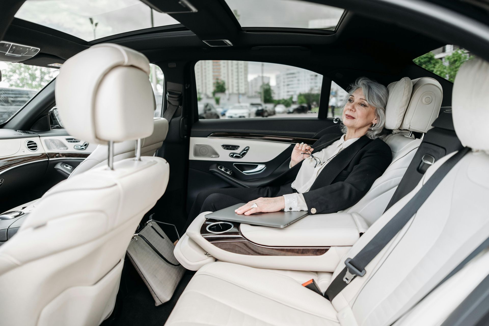 Woman in a business suit working on a laptop inside a luxury car with cream leather seats.