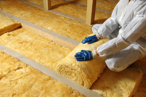 A person is kneeling on the floor holding a roll of insulation.