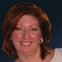 Woman with reddish-brown hair smiles, wearing earrings, against a blue background.