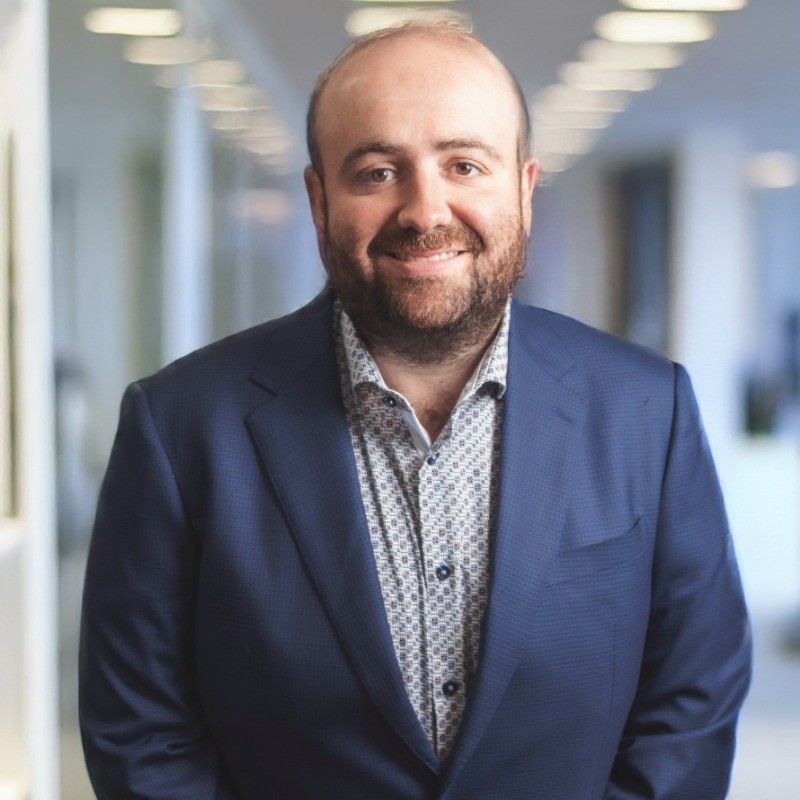 Man in a blue suit smiling, indoors in an office setting.