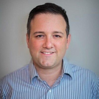 Man smiling, wearing a blue striped button-down shirt, neutral background.