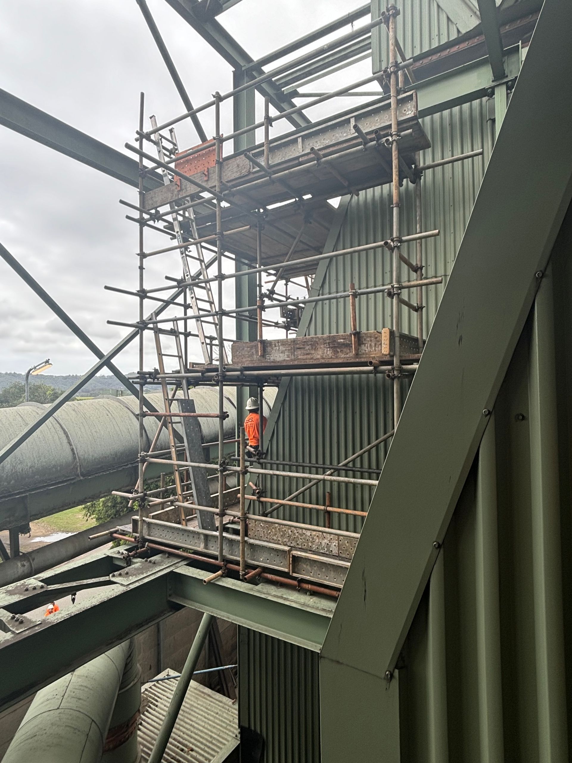 Construction scaffolding set up on an industrial building, with a worker in a hi-vis vest and hard hat standing on a platform. — Lennox Head Scaffolding in Murwillumbah, NSW