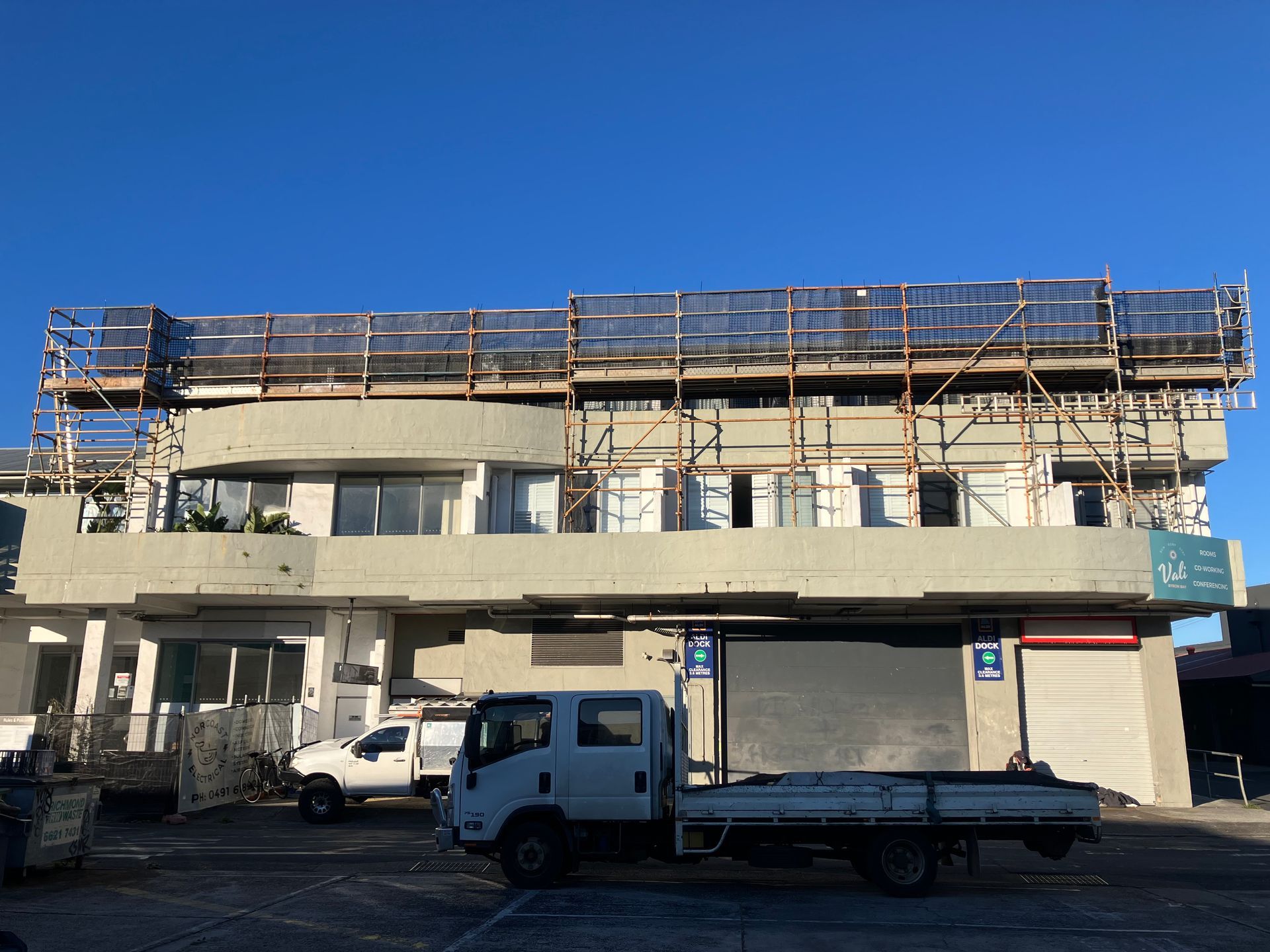 Building under renovation with scaffolding and work trucks in Byron Bay. — Lennox Head Scaffolding in Byron Bay, NSW